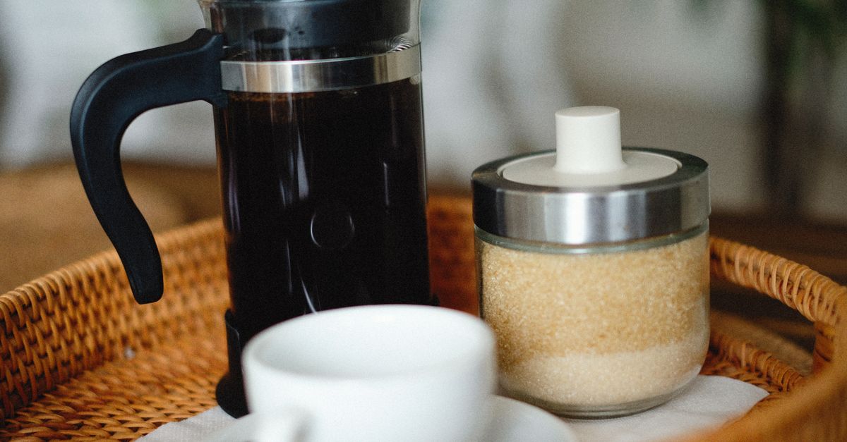 Close-up of a French press, sugar jar, and coffee cup on a wicker tray.
