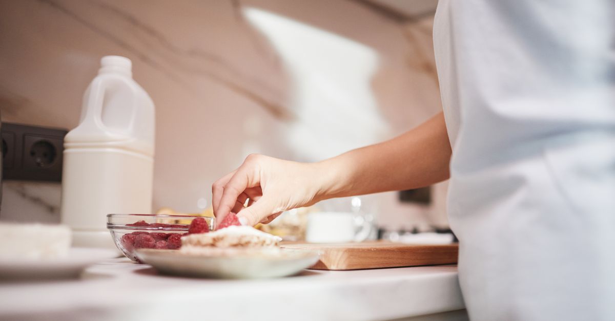 A close-up of a person preparing a raspberry dish on a kitchen counter.