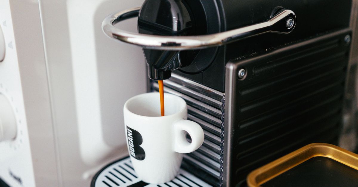 Close-up of a modern coffee machine brewing espresso into a branded mug indoors.